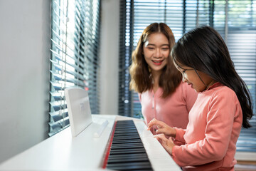 Asian attractive mother teach daughter play piano in living room at home. 