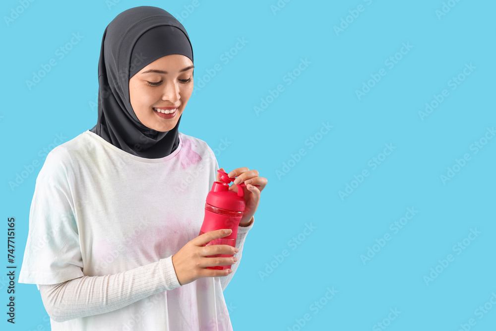 Sticker Sporty Muslim woman with bottle of water on blue background