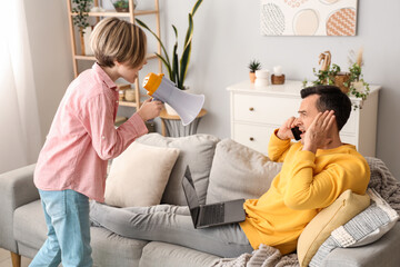 Noisy little boy shouting into megaphone and his busy father at home