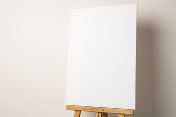 A blank white canvas is mounted on a wooden easel, with copy space