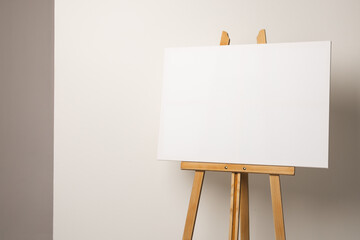 A blank canvas rests on a wooden easel against a neutral background, with copy space
