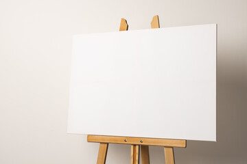 A blank canvas is positioned on a wooden easel against a neutral background, with copy space