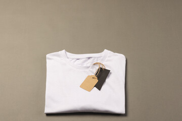 A plain white t-shirt with a blank tag attached lies on a neutral background, with copy space