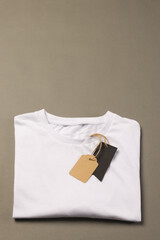 A folded white t-shirt with a blank tag attached to it lies on a neutral background, with copy space