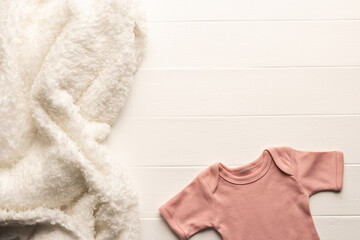 A soft, cozy white blanket lies next to a tiny pink baby onesie on a white wooden background, with c