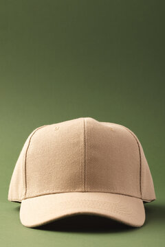 A beige baseball cap is positioned against a green background, with copy space