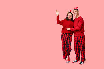 Happy young couple in Christmas pajamas on pink background