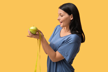 Beautiful young woman with measuring tape and fresh apple on yellow background. Weight loss concept