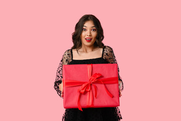 Beautiful young shocked Asian woman with gift box on pink background. Valentine's Day celebration
