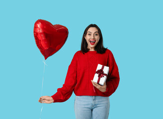 Beautiful young happy woman with gift box and heart-shaped balloon on blue background. Valentine's...