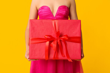 Beautiful young woman with gift box on yellow background. Valentine's Day celebration