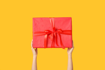 Female hands with gift box on yellow background. Valentine's Day celebration