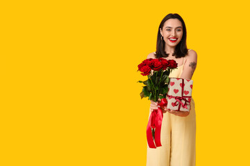 Beautiful young happy woman with gift box and bouquet of roses on yellow background. Valentine's Day celebration