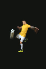 Fototapeta premium Young man playing with soccer ball in motion on black background
