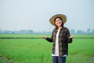 Asian female farmer dressed in brown shirt, jeans Stand and pose at a green rice field.