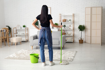 Young woman with floor mop and bucket in living room, back view - obrazy, fototapety, plakaty