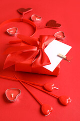 Composition with gift box, blank card and candles for Valentine's Day celebration on red background