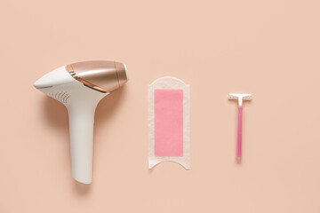 Modern photoepilator with razor and wax strip on beige background