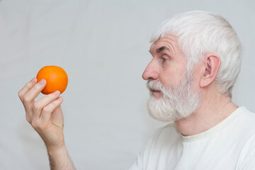 A gray-haired elderly man holds a tangerine in his hands
