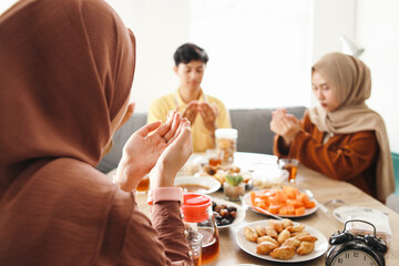 Group of young muslim boy and girl praying before eating iftar food together at home on Ramadan Month 