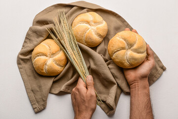 Male hands with delicious kaiser rolls and wheat ears on napkin against white background