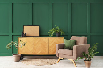 Interior of living room with armchair, cushion and chest of drawers near green wall