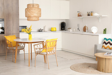 Interior of cozy stylish kitchen studio with table, mimosa flowers, armchairs and counters