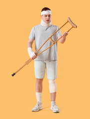 Injured young man after accident with crutch on yellow background