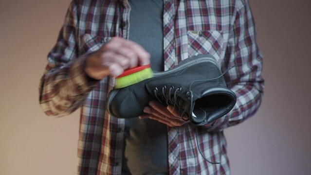 Man cleaning black boots with brushes in the studio. Male brushing nubuck footwear with a small scrub brush. Theme of care for winter shoes. Washes dirty black fall booties, workshop shoes cleaner. 