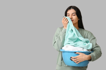 Beautiful young woman holding basket with clean laundry on grey background