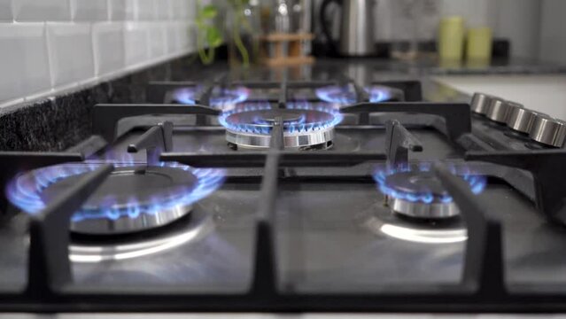 Paneo vertical de cinco hornallas encendidas de estufa a gas natural en contexto de cocina moderna