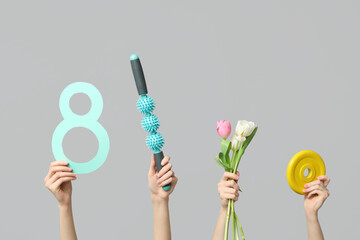 Female hands with paper figure 8, sports equipment and tulips for International Women's Day on grey background