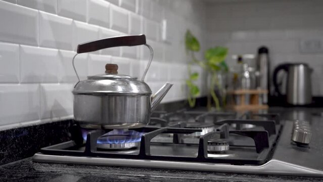Pava hirviendo emanando vapor de agua sobre estufa a gas natural con fondo de hermosa cocina moderna