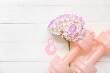 Paper figure 8, dumbbells and flowers on light wooden background. International Women's Day