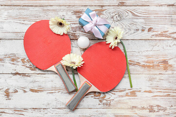 Composition with ping pong rackets, gift box and flowers on light wooden background. International...