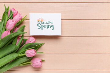 Greeting card with text WELCOME SPRING and beautiful tulips on pink wooden background