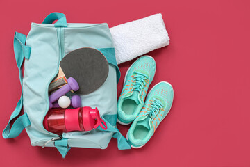Sports bag with sportswear, water and ping pong equipment on red background
