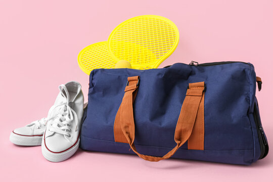 Sports bag with sportswear, tennis rackets and shoes on pink background