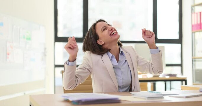 Excited businesswoman sitting at table and experiencing euphoria in office