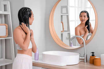 Obraz premium Young Asian woman applying hair mask near mirror in bathroom