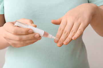 Woman applying cuticle oil with pen on white background, closeup