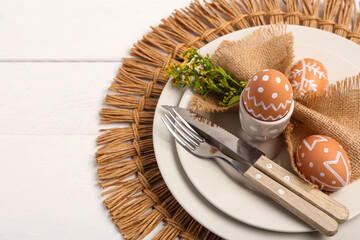 Beautiful table setting with Easter eggs and yellow flowers on white wooden background