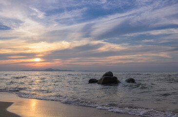 Fototapeta na wymiar Ocean at sunset with sun reflection on sand and rocks on sea.