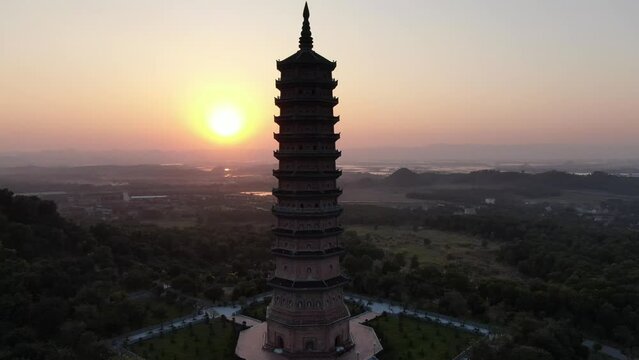 Drone aerial view in Vietnam flying around a buddhist pagoda in a Ninh Binh temple at sunset with green landscape in the horizon
