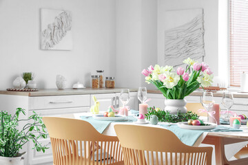 Festive Easter table setting with vase of flowers, cutlery, napkins and painted eggs in kitchen