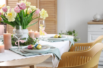 Festive Easter table setting with vase of flowers, cutlery, candles and painted eggs