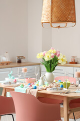Stylish Easter table setting and vase of flowers in room