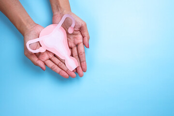 Female reproductive health concept. Woman hand holding uterus shape made from paper on blue background.