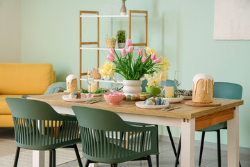 Light interior of festive dining room with Easter table setting, vase of flowers and chairs
