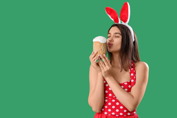 Beautiful young woman in bunny ears with Easter cake on green background